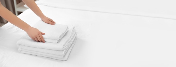 Image of Woman putting clean white towels on bed, closeup with space for text. Banner design