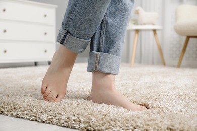 Photo of Woman standing on soft carpet at home, closeup