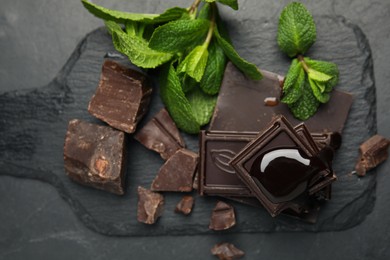 Photo of Tasty chocolate pieces with syrup and mint on black table, flat lay