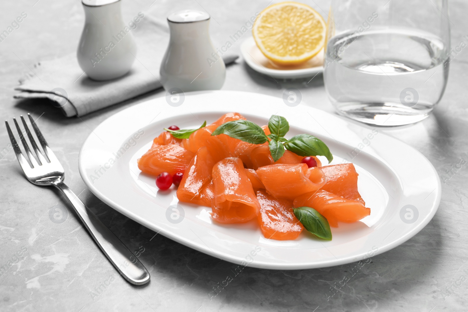 Photo of Salmon carpaccio with cranberries and basil served on grey table