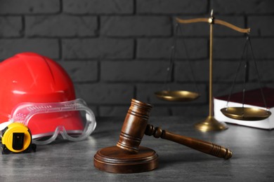 Photo of Construction and land law concepts. Gavel, scales of justice, hard hat, protective goggles and measuring tape on gray table against brick wall