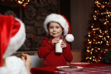 Photo of Cute little child with glass of milk at table in dining room. Christmas time