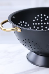 Photo of Black colander on white marble table indoors, closeup