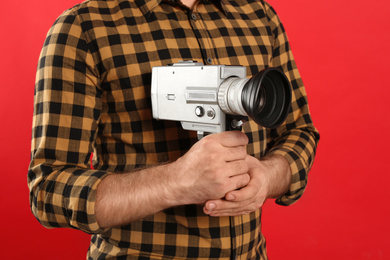 Young man with vintage video camera on red background, closeup