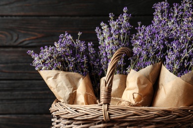 Photo of Fresh lavender flowers in basket against dark wooden background, closeup view