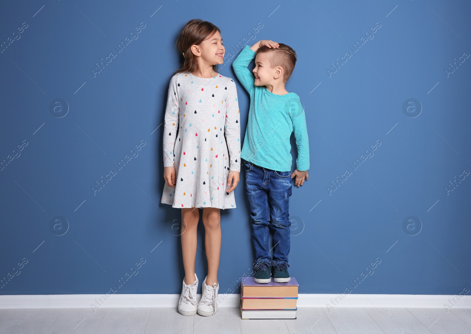 Photo of Little girl and boy measuring their height near color wall