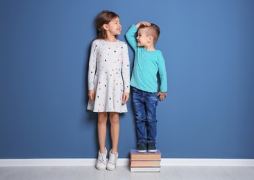 Photo of Little girl and boy measuring their height near color wall