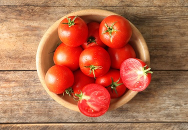 Photo of Fresh ripe tomatoes in bowl on wooden table, top view