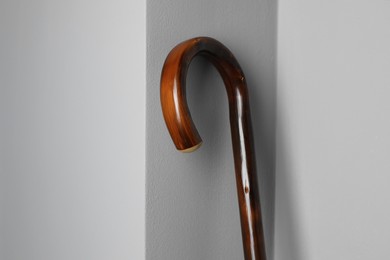 Photo of Elegant wooden walking cane near light grey wall, closeup. Space for text