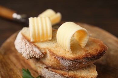 Photo of Tasty butter curls and slices of bread on wooden table, closeup