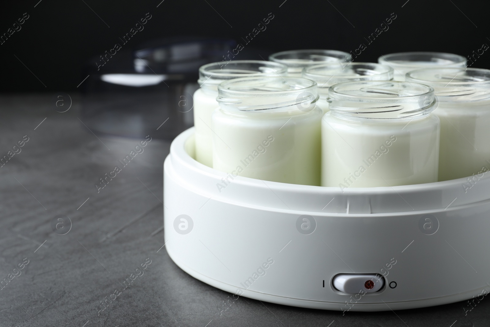 Photo of Modern yogurt maker with full jars on grey table. Space for text