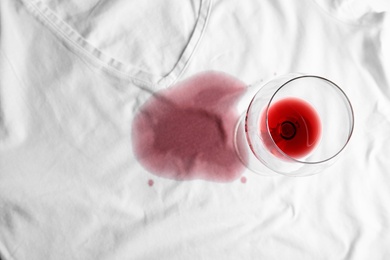 Photo of Transparent glass and spilled exquisite red wine on white t-shirt, top view. Space for text