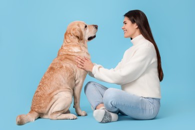 Photo of Happy woman with cute Labrador Retriever on light blue background