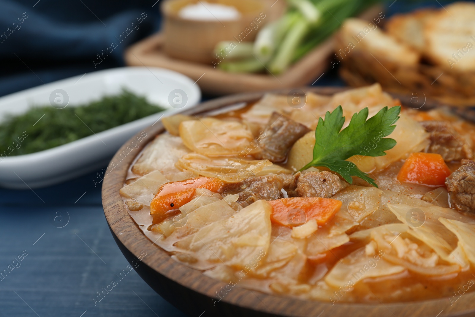 Photo of Tasty cabbage soup with meat, carrot and parsley on blue wooden table, closeup