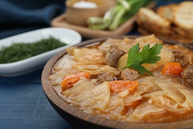 Tasty cabbage soup with meat, carrot and parsley on blue wooden table, closeup