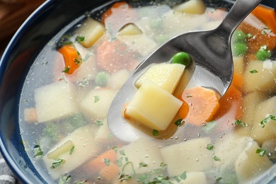 Photo of Spoon of fresh homemade vegetable soup over full bowl, closeup