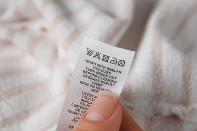 Woman reading clothing label with care symbols on striped shirt, closeup