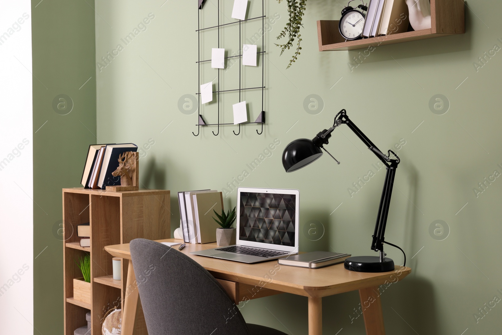 Photo of Modern laptop, books, lamp and stationery on wooden desk near green wall. Home office