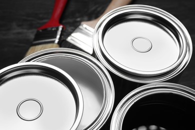 Photo of Cans of white and black paints with brushes on table, closeup