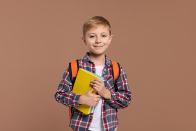 Photo of Happy schoolboy with backpack and books on brown background