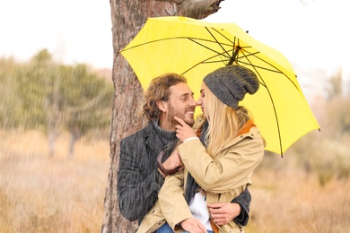 Photo of Young romantic couple with umbrella in park on autumn day