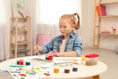 Cute little child painting at table in room