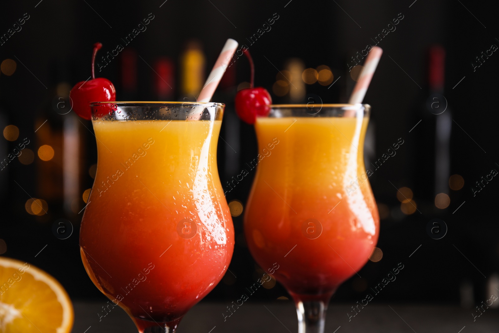 Photo of Fresh alcoholic Tequila Sunrise cocktails against blurred lights, closeup