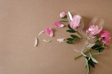 Photo of Wineglasses and beautiful pink peonies on brown background, flat lay. Space for text