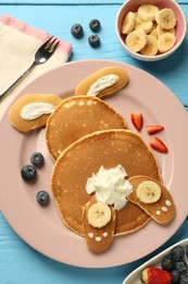 Photo of Creative serving for kids. Plate with cute bunny made of pancakes, berries, cream and banana on light blue wooden table, flat lay