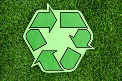 Photo of Paper recycling symbol on green grass, top view