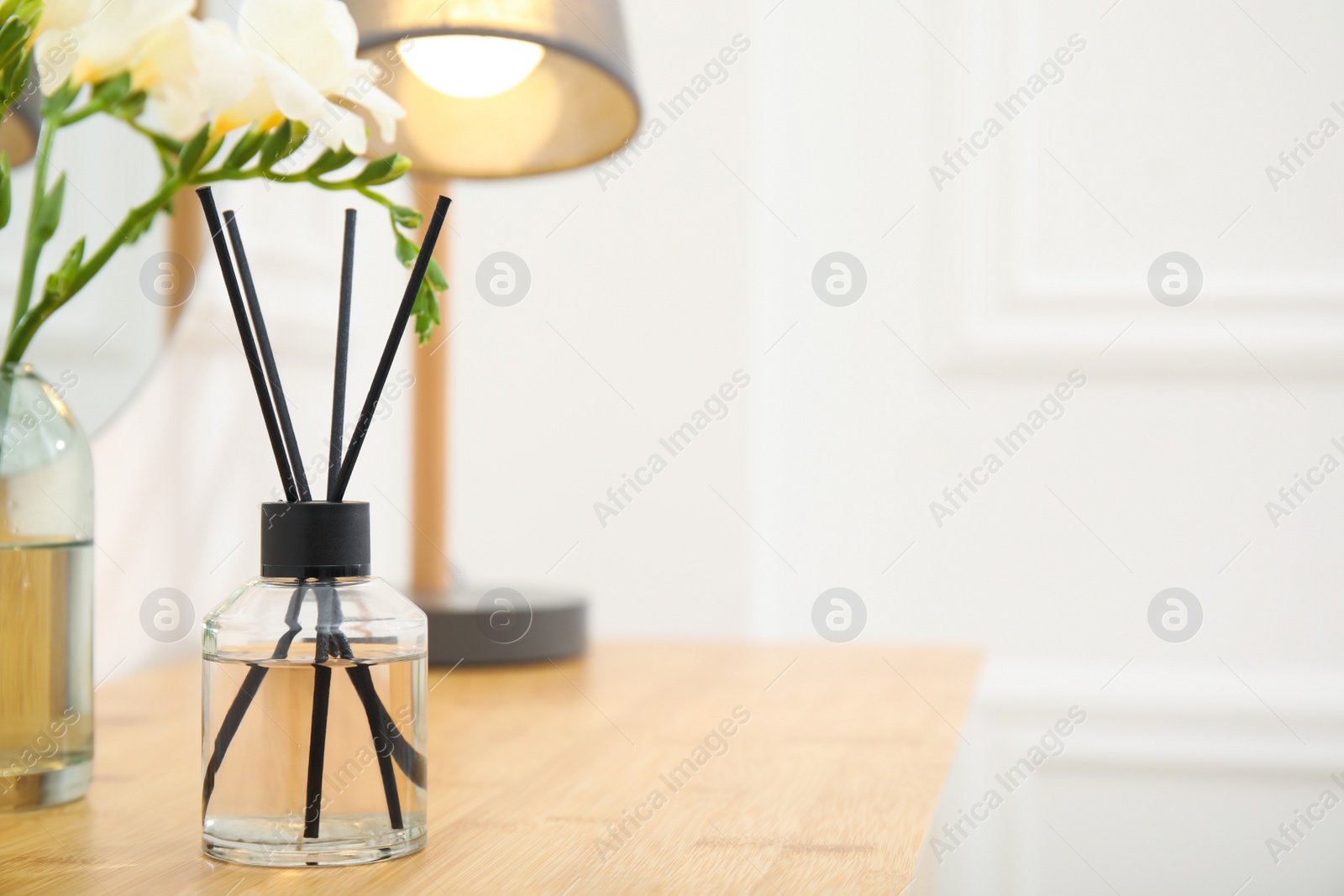 Photo of Aromatic reed air freshener and flowers on wooden table in room. Space for text