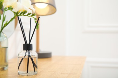 Photo of Aromatic reed air freshener and flowers on wooden table in room. Space for text