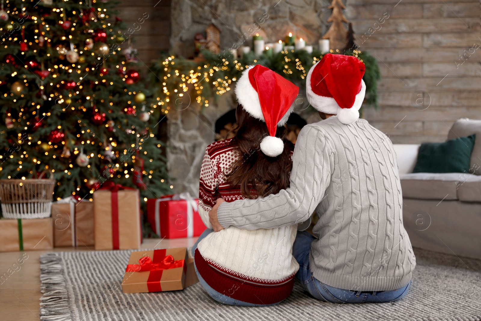 Photo of Happy young couple wearing Santa hats in living room decorated for Christmas