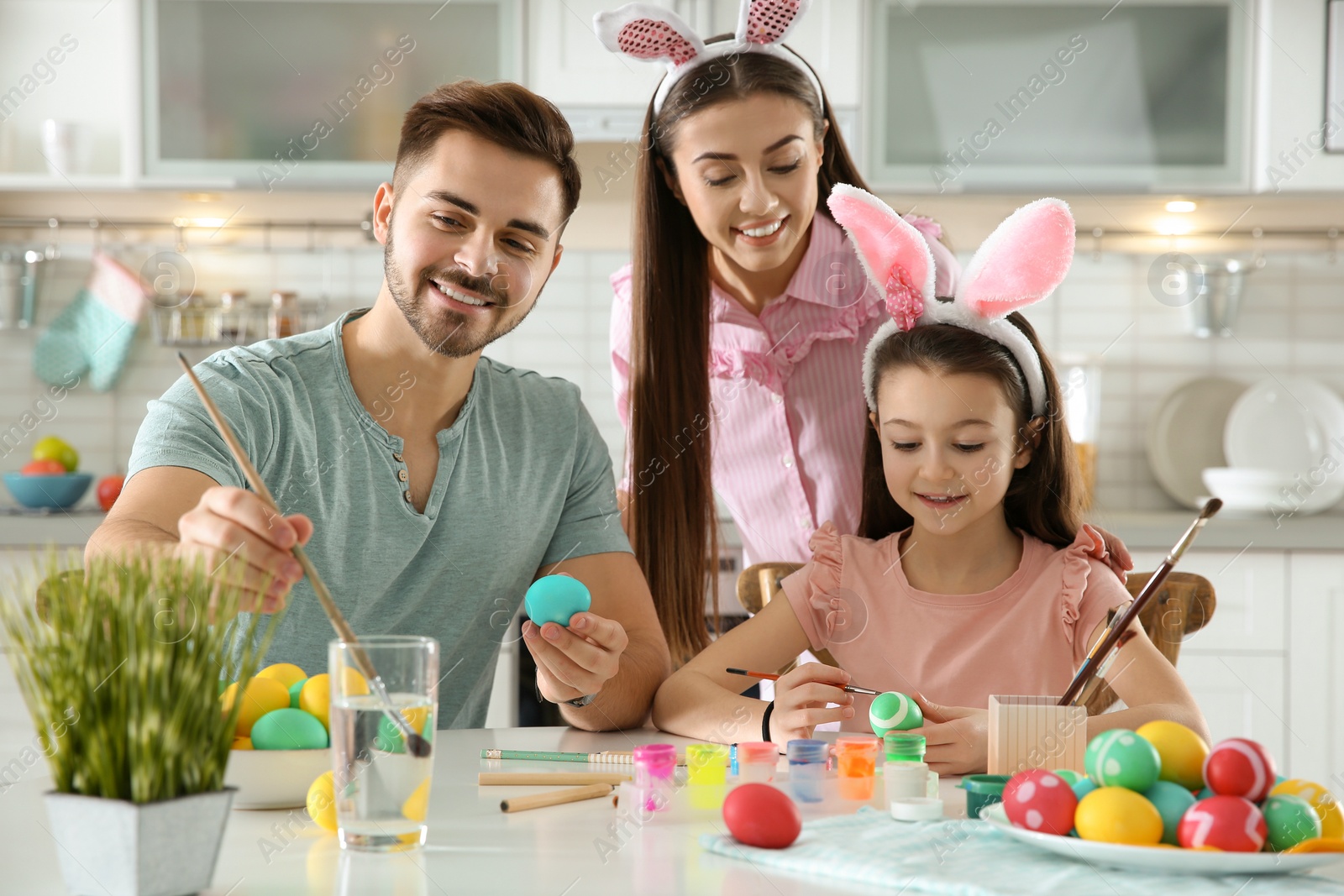 Photo of Father, mother and daughter painting Easter eggs in kitchen