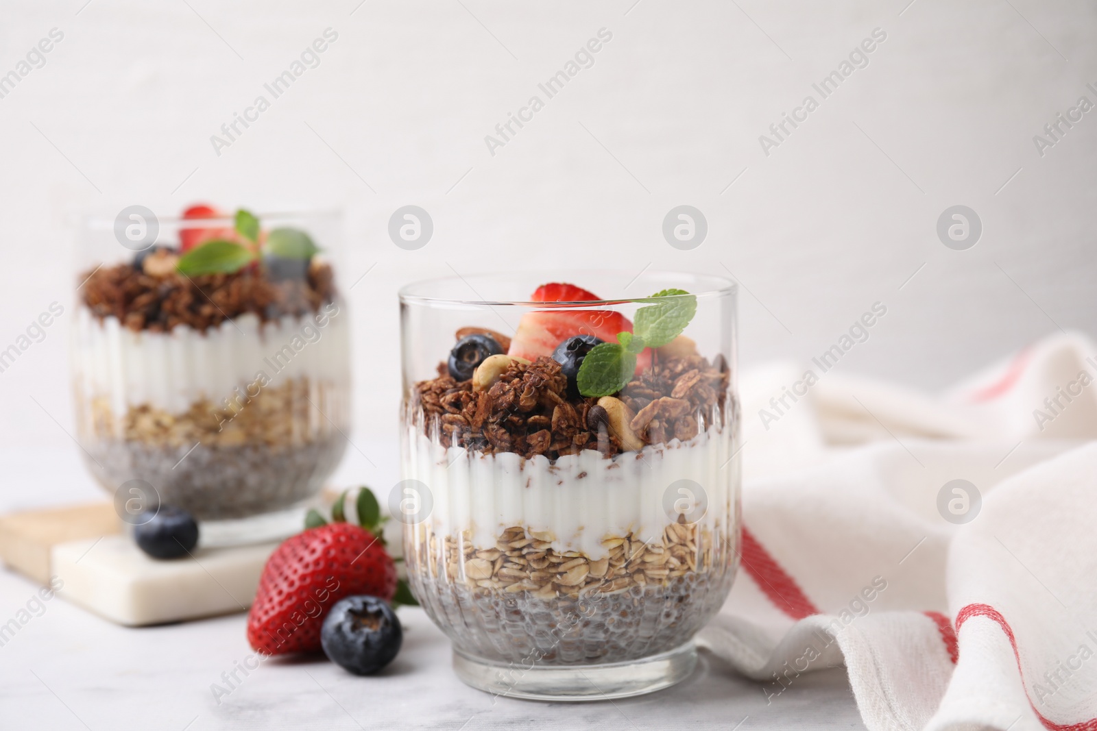 Photo of Tasty granola with berries, nuts, yogurt and chia seeds in glasses on white table