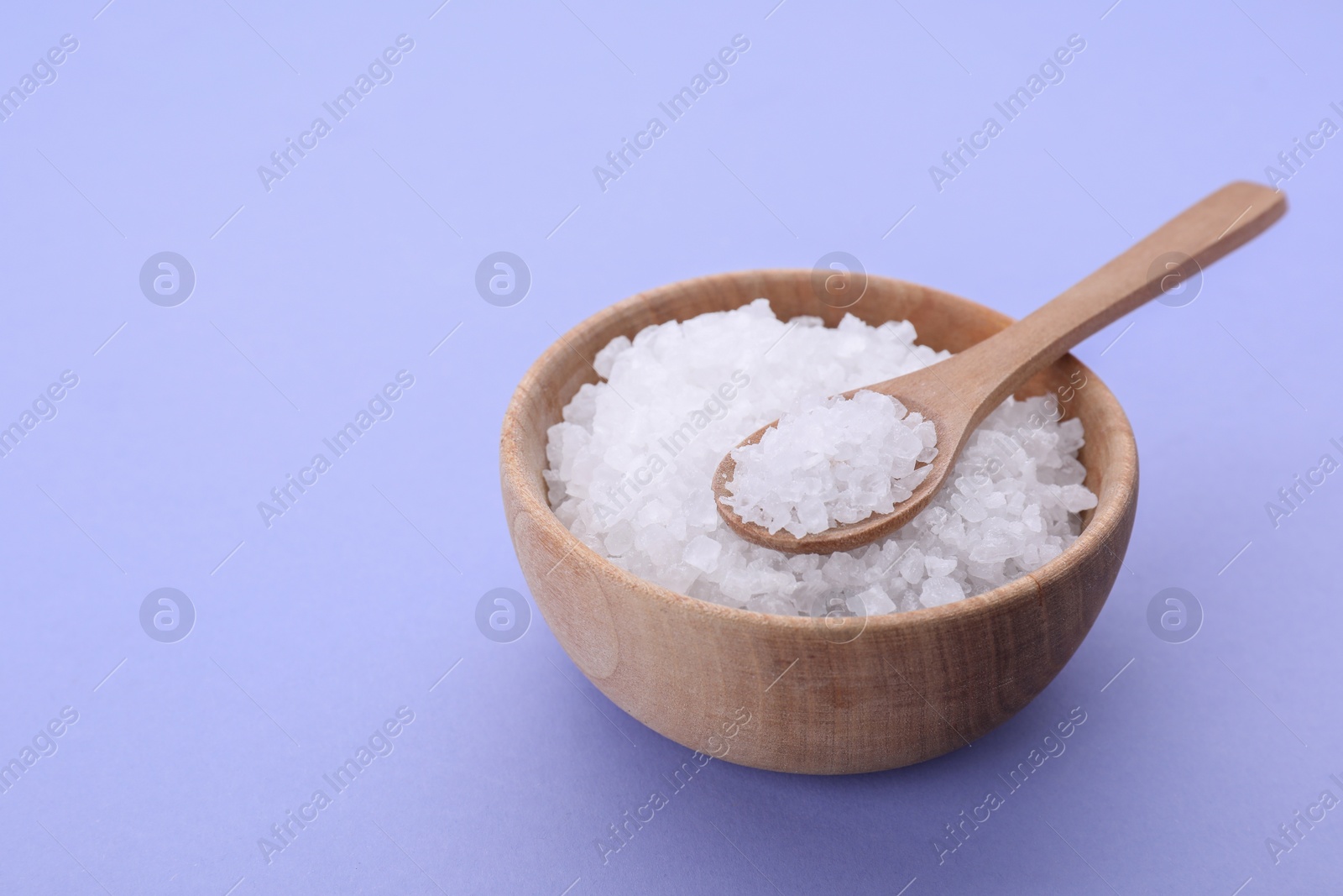 Photo of Bowl and spoon with sea salt on violet background, space for text