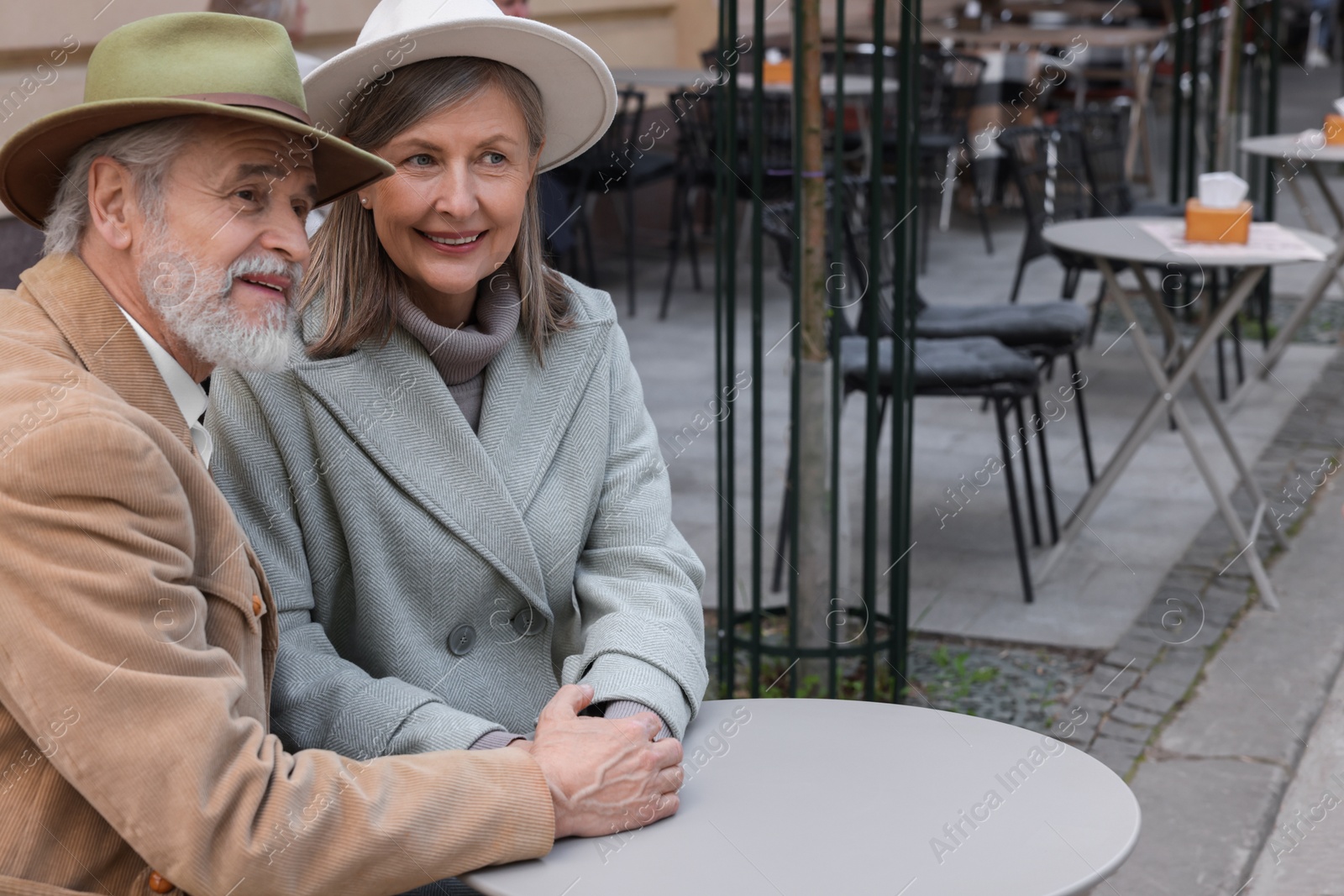 Photo of Portrait of affectionate senior couple sitting in outdoor cafe, space for text