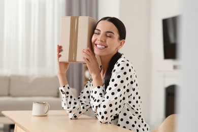 Happy young woman with parcel at table indoors. Internet shopping