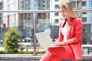 Photo of Beautiful businesswoman with laptop on city street. Space for text