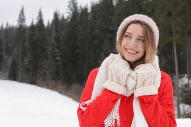 Happy young woman in warm clothes outdoors, space for text. Winter vacation