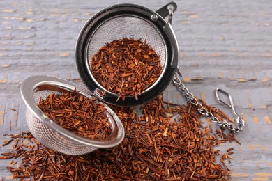 Photo of Infuser with dry rooibos leaves on grey wooden table, closeup