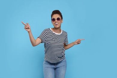 Photo of Happy young woman in stylish sunglasses dancing on light blue background