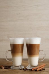 Hot coffee with milk in glass cups, beans and cinnamon sticks on wooden table