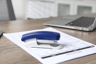 Photo of Bright stapler and document on wooden table indoors