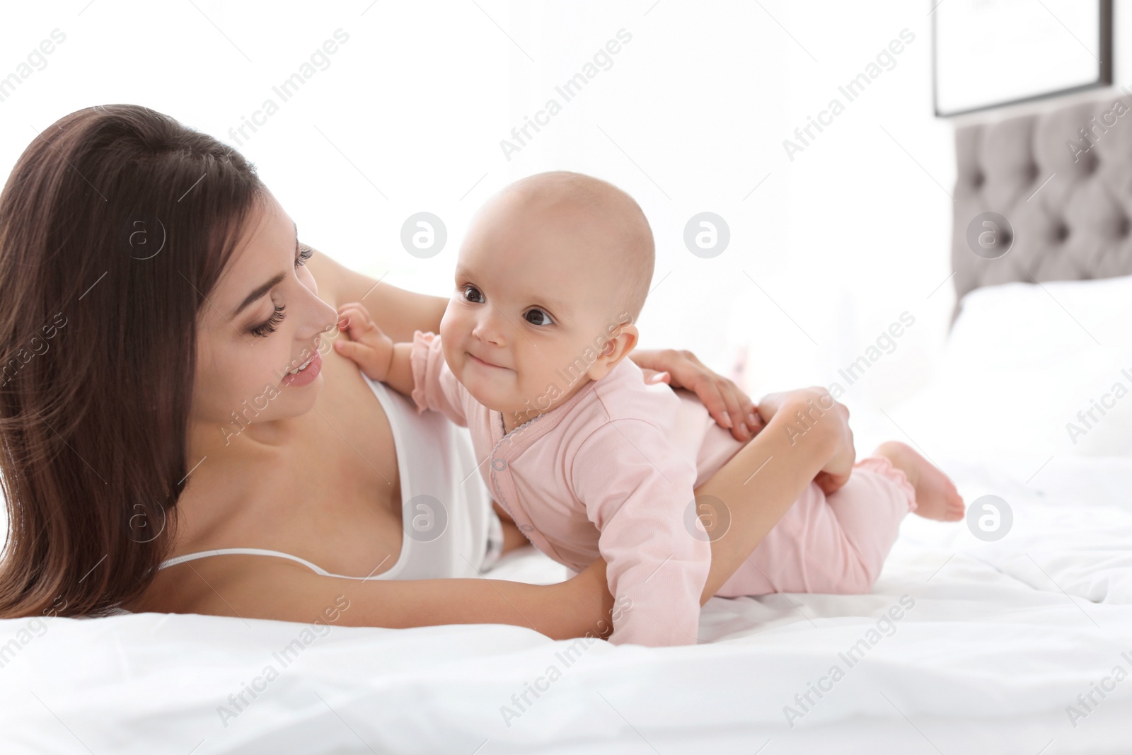 Photo of Young mother with her cute baby girl on bed at home