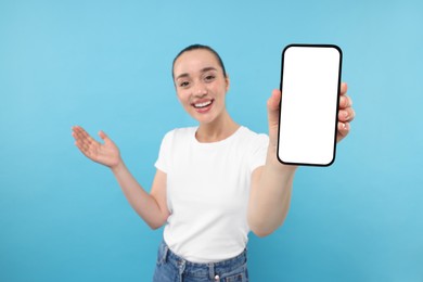 Photo of Young woman showing smartphone in hand on light blue background, selective focus. Mockup for design