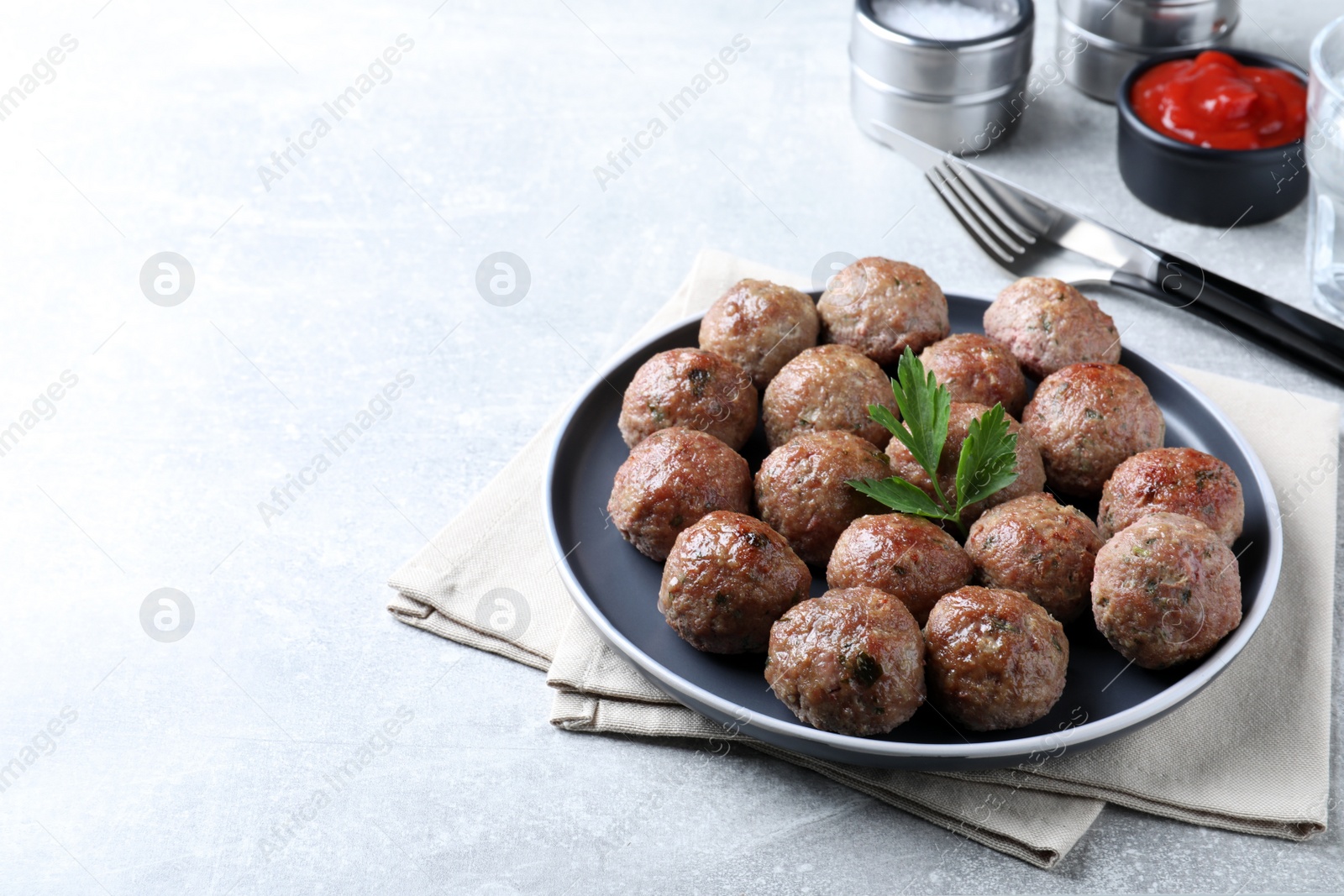 Photo of Tasty cooked meatballs with parsley served on light grey table. Space for text