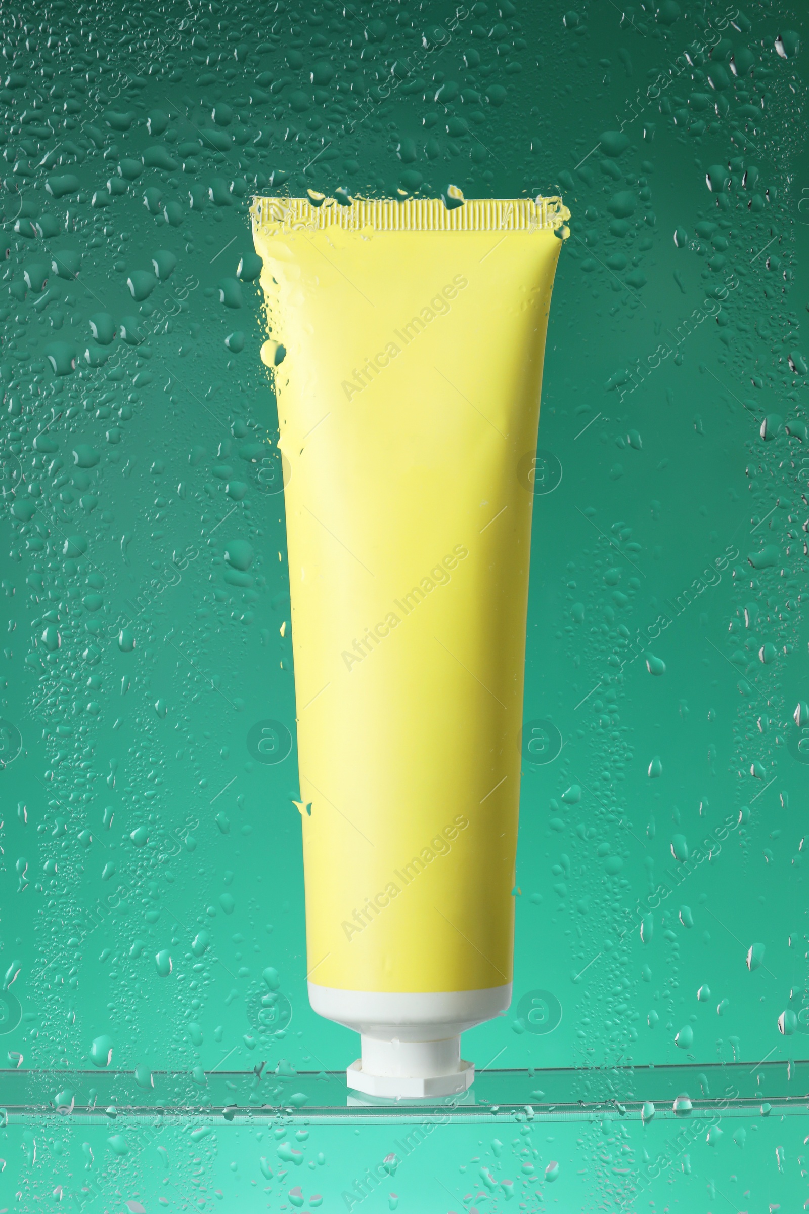 Photo of Tube with moisturizing cream on green background, view through wet glass