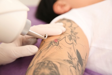 Photo of Young woman undergoing laser tattoo removal procedure in salon, closeup