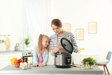 Photo of Mother and daughter preparing food with modern multi cooker in kitchen